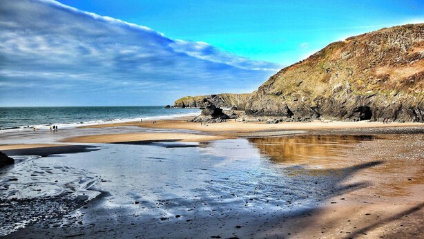 Ein Strand mit felsigen Klippen, ruhigem Wasser und blauem Himmel.