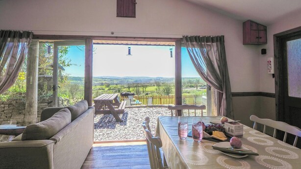 A room with a view of a garden, a dining table with a tablecloth, and a sofa.