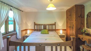 A bedroom with a wooden bed frame, a single bed with a green pillow, two bedside lamps, a wooden wardrobe, and a window with curtains.