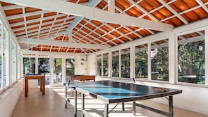 Un espacio interior amplio con mesa de ping pong, ventanas grandes y estructura de techo de madera.