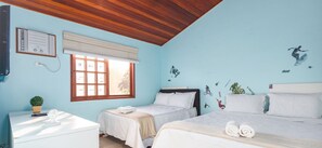 Una habitación con dos camas, techo de madera, ventana con persianas, una mesita con una planta y adornos en la pared.
