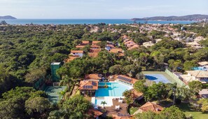 Vista aérea de un complejo turístico con piscina, rodeado de exuberante vegetación y un paisaje costero.