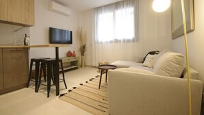 A modern living room with a sofa, a coffee table, a TV, and a kitchen area with a bar stool.