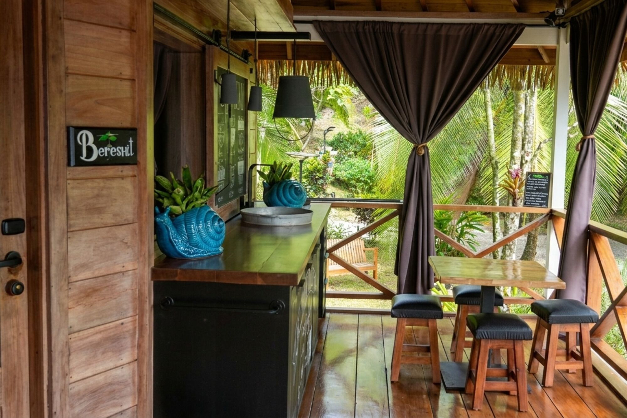 Una cabaña de madera con una zona de bar, un letrero que dice 'Bereshit' y vistas de la vegetación tropical.