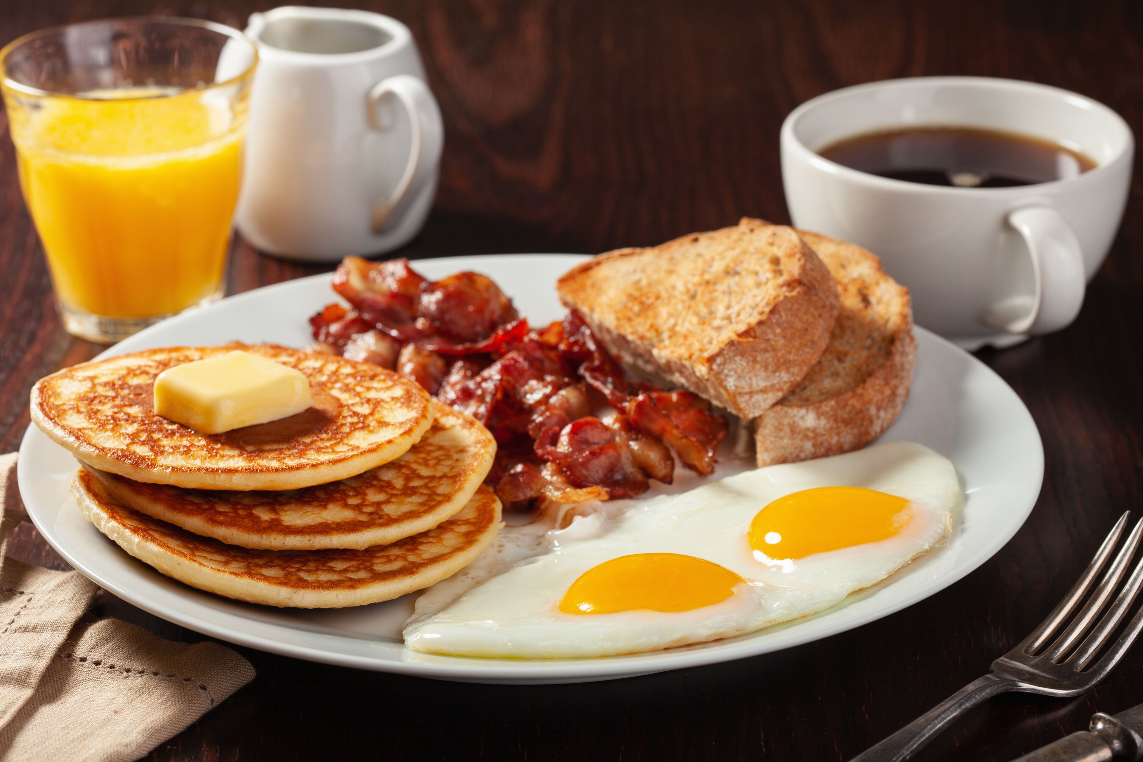 A breakfast plate with pancakes, bacon, eggs, toast, and butter.