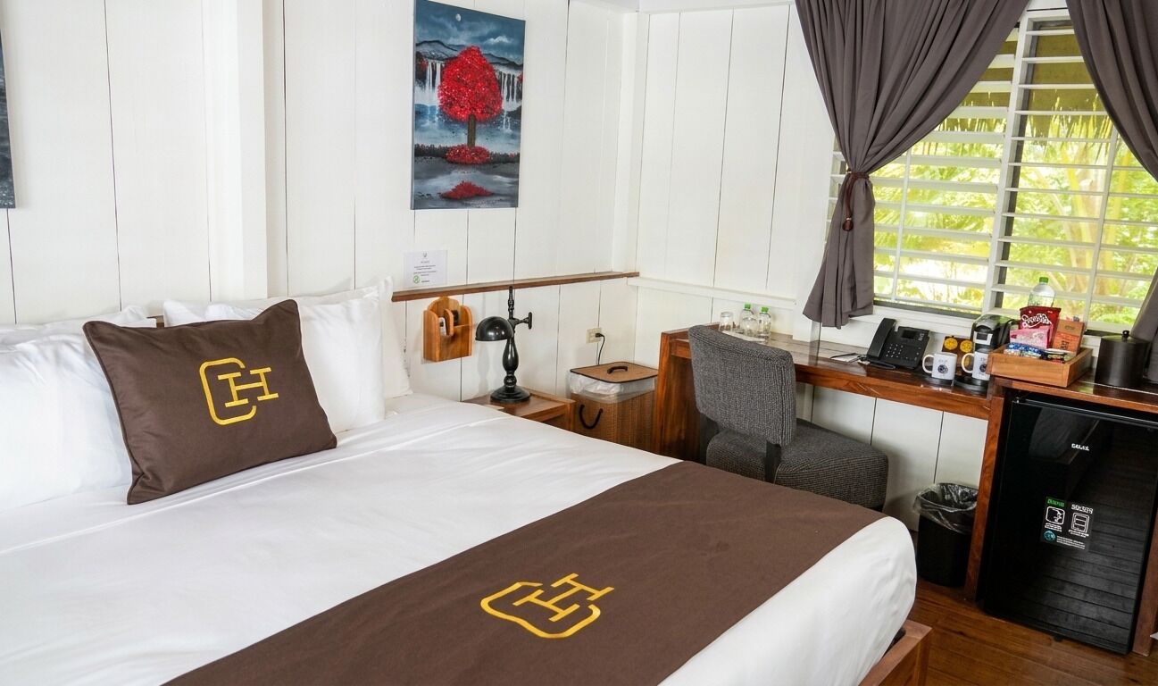 A hotel room with a bed, a desk, a chair, a small refrigerator, and a window with curtains.