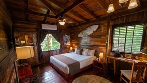 A wooden cabin bedroom with a bed, desk, chair, and a window with blinds.