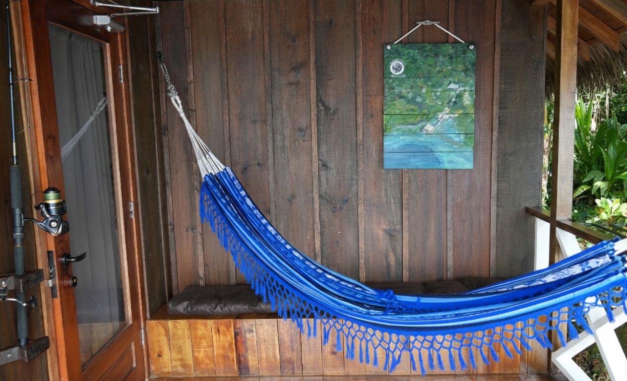 Un hamac suspendu entre des poutres en bois, une porte en bois et un tableau encadré accroché au mur.