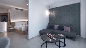 A modern living room with a grey sofa, a small round table, and a bed with a wooden headboard. - Athens City Suites (Athens)