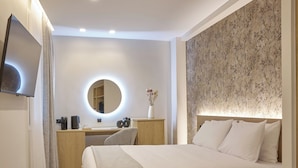 A modern hotel room with a large bed, a desk with a computer, a round mirror, and a TV mounted on the wall. - Athens City Suites (Athens)
