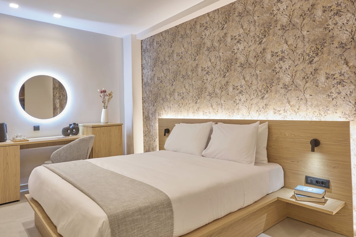 Quarto moderno com uma cama grande, uma mesinha de cabeceira com abajur, um espelho redondo e papel de parede com padrão floral.
