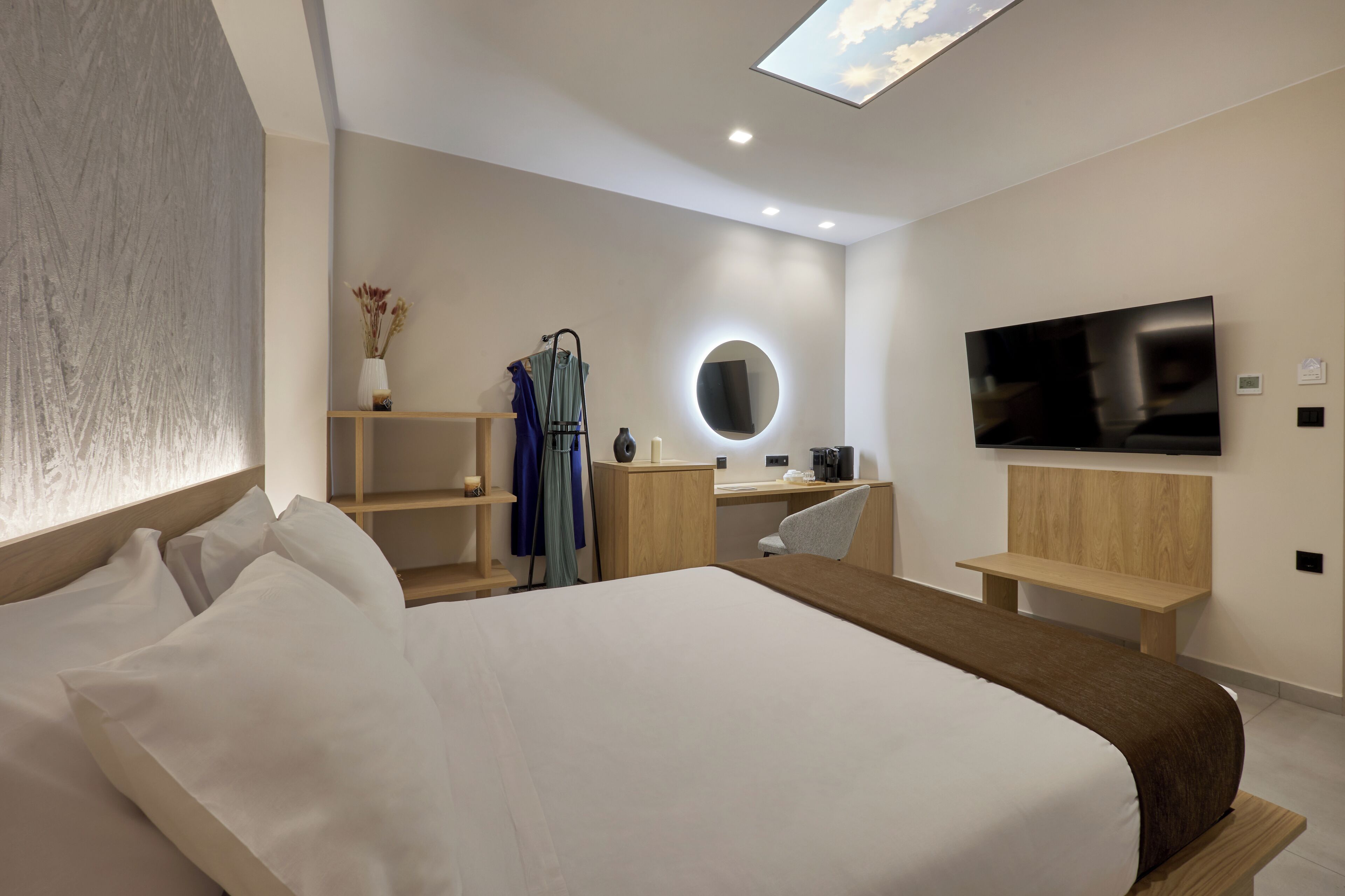 A modern hotel room with a large bed, a desk, a chair, a TV, and a skylight.