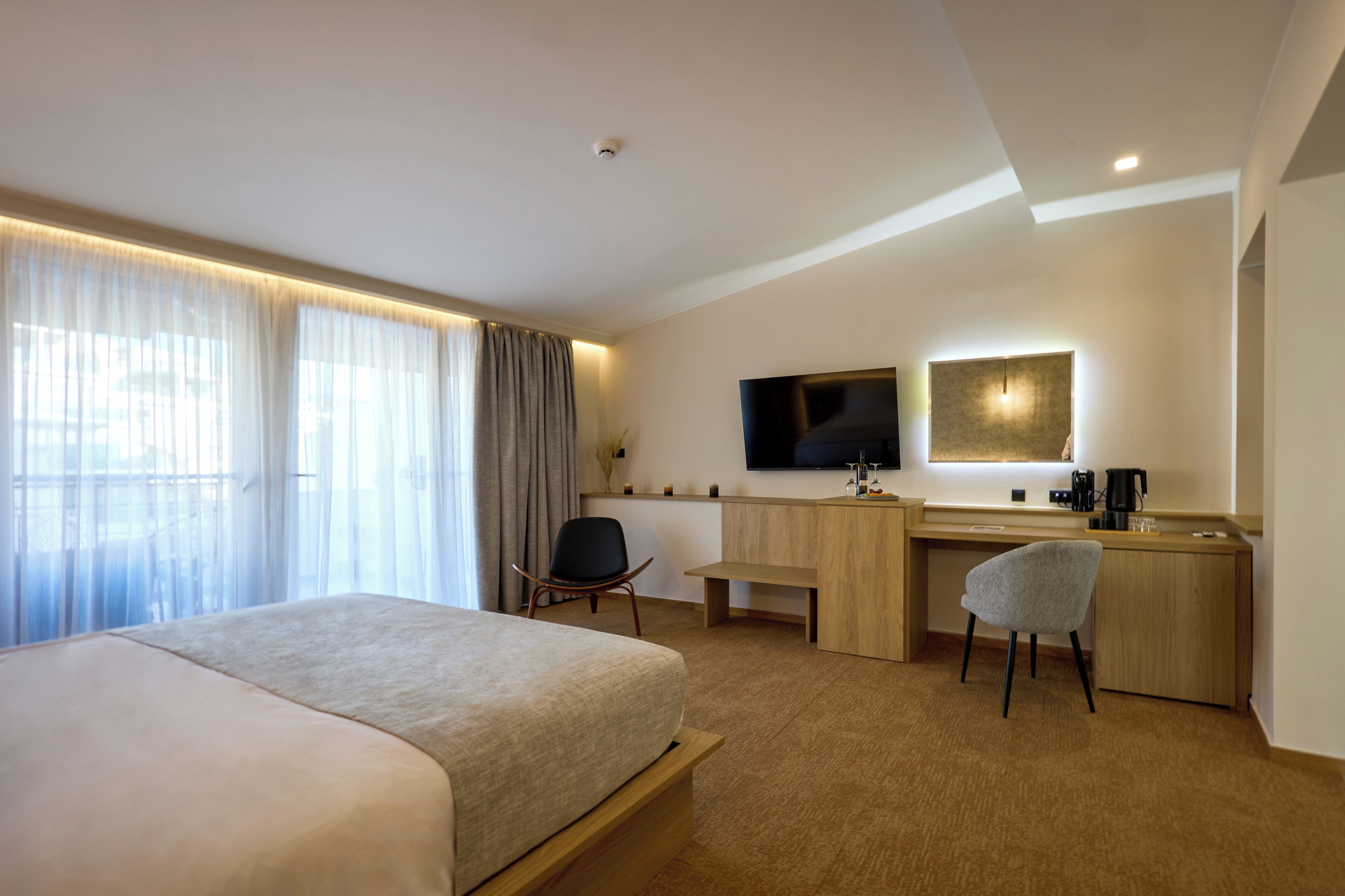 A hotel room with a bed, desk, chair, TV, and a coffee machine.