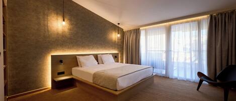 A modern hotel room with a large bed, a wooden headboard, a bedside table, and a chair.