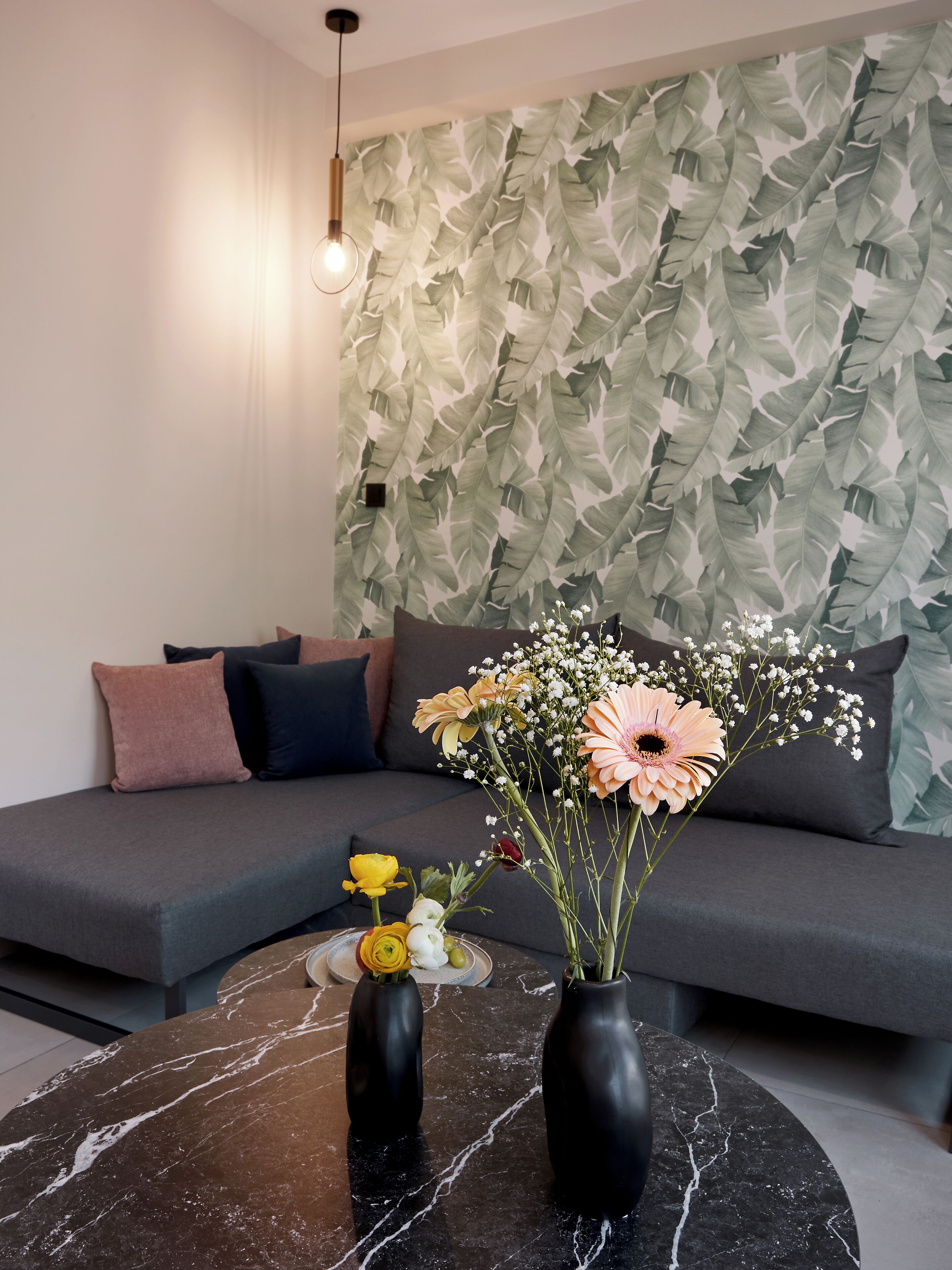 A modern living room with a grey sofa, a black marble coffee table, and a wall with a leafy pattern.