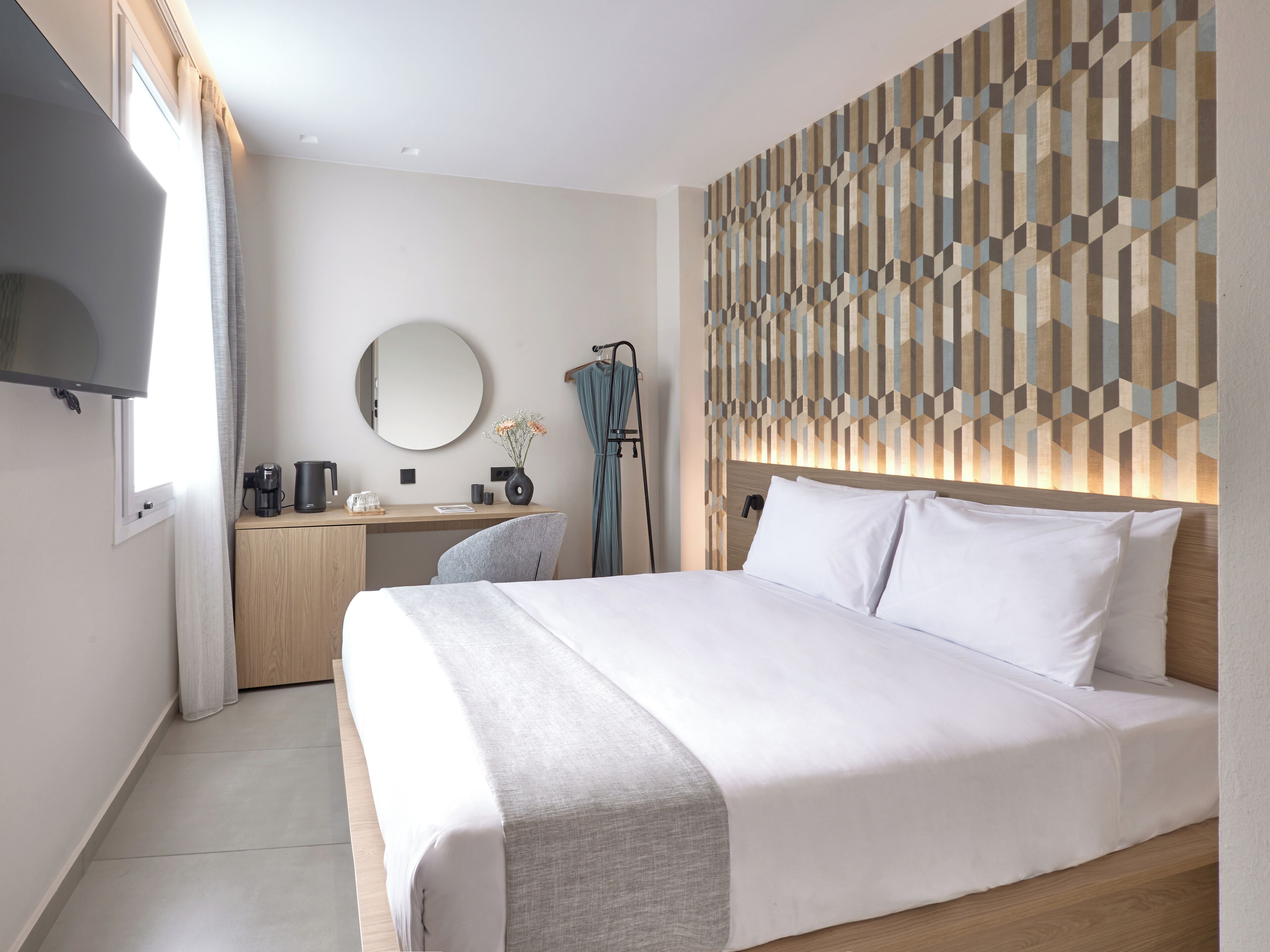 Habitació d'hotel moderna amb un llit gran, una taula de treball amb cadira, televisió de pantalla plana, mirall rodó i paret amb disseny.