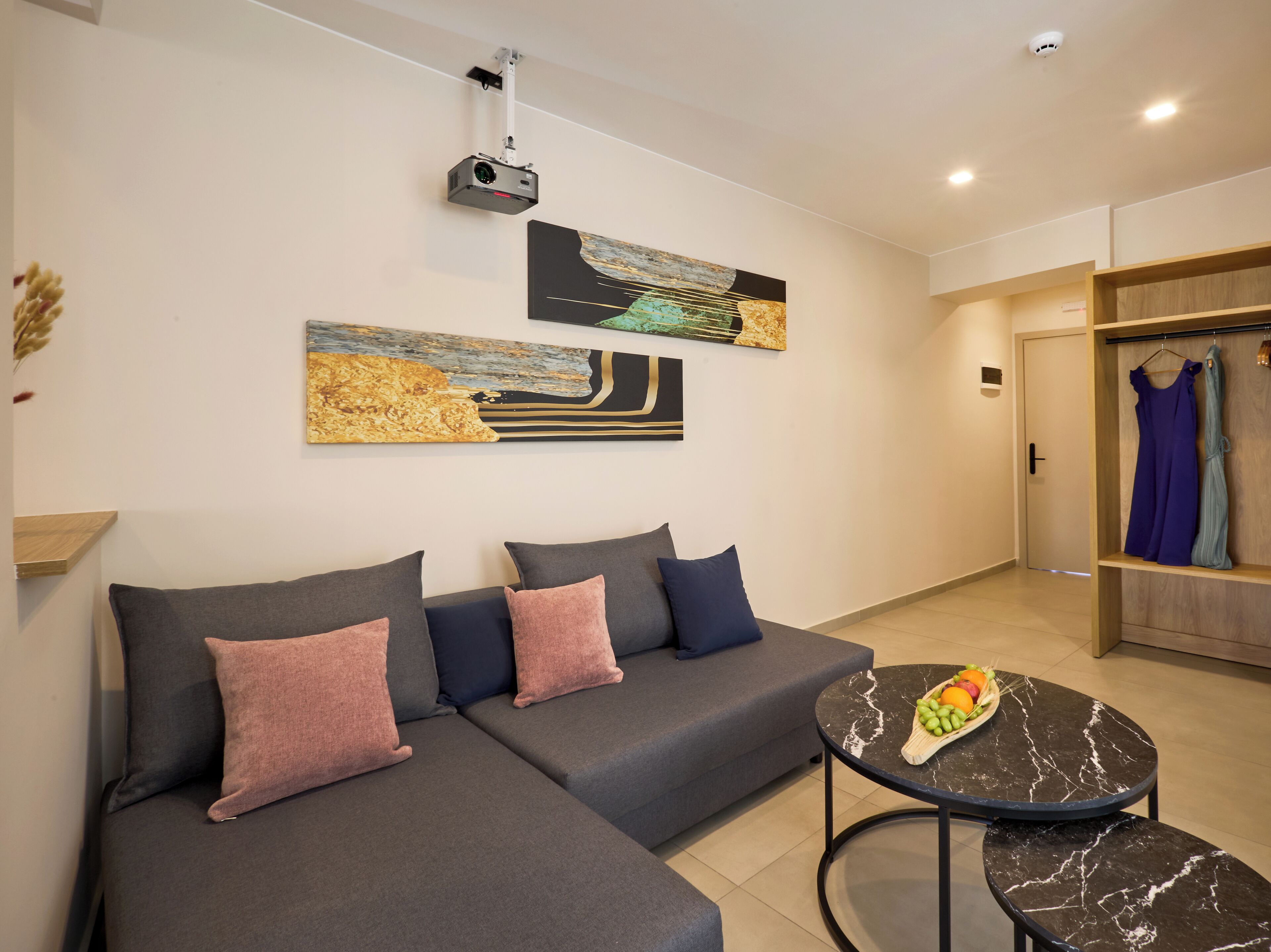 A modern living room with a grey sectional sofa, a round black marble coffee table with fruit, and abstract wall art.