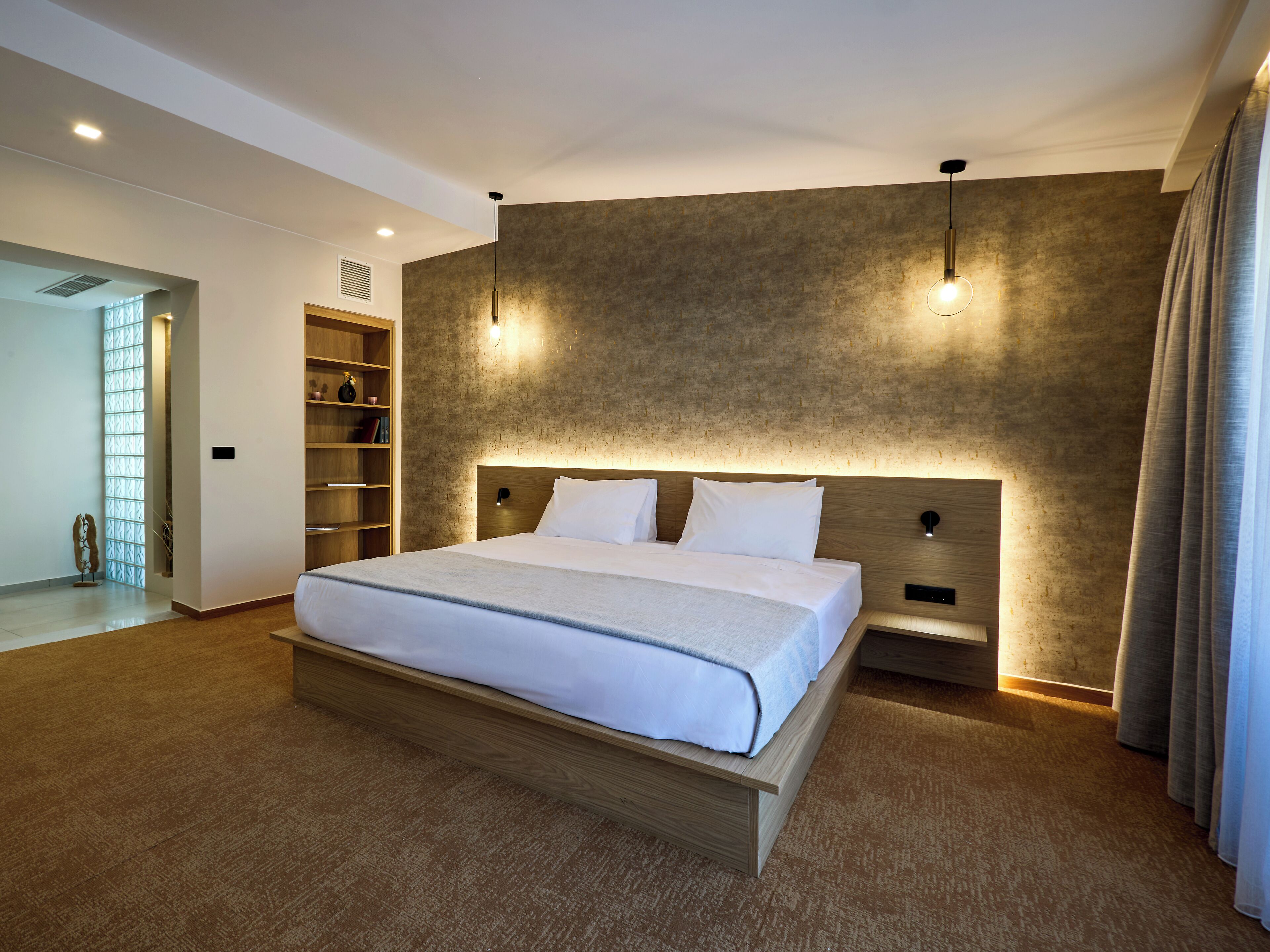 A modern hotel room with a large bed, built-in shelving, and a textured wall.