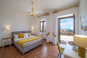 A bedroom with a bed, bedside tables, a chandelier, curtains, a balcony with a view, and a dining table with a lamp. - IL vigneto di nonno Pietro (Pianillo)