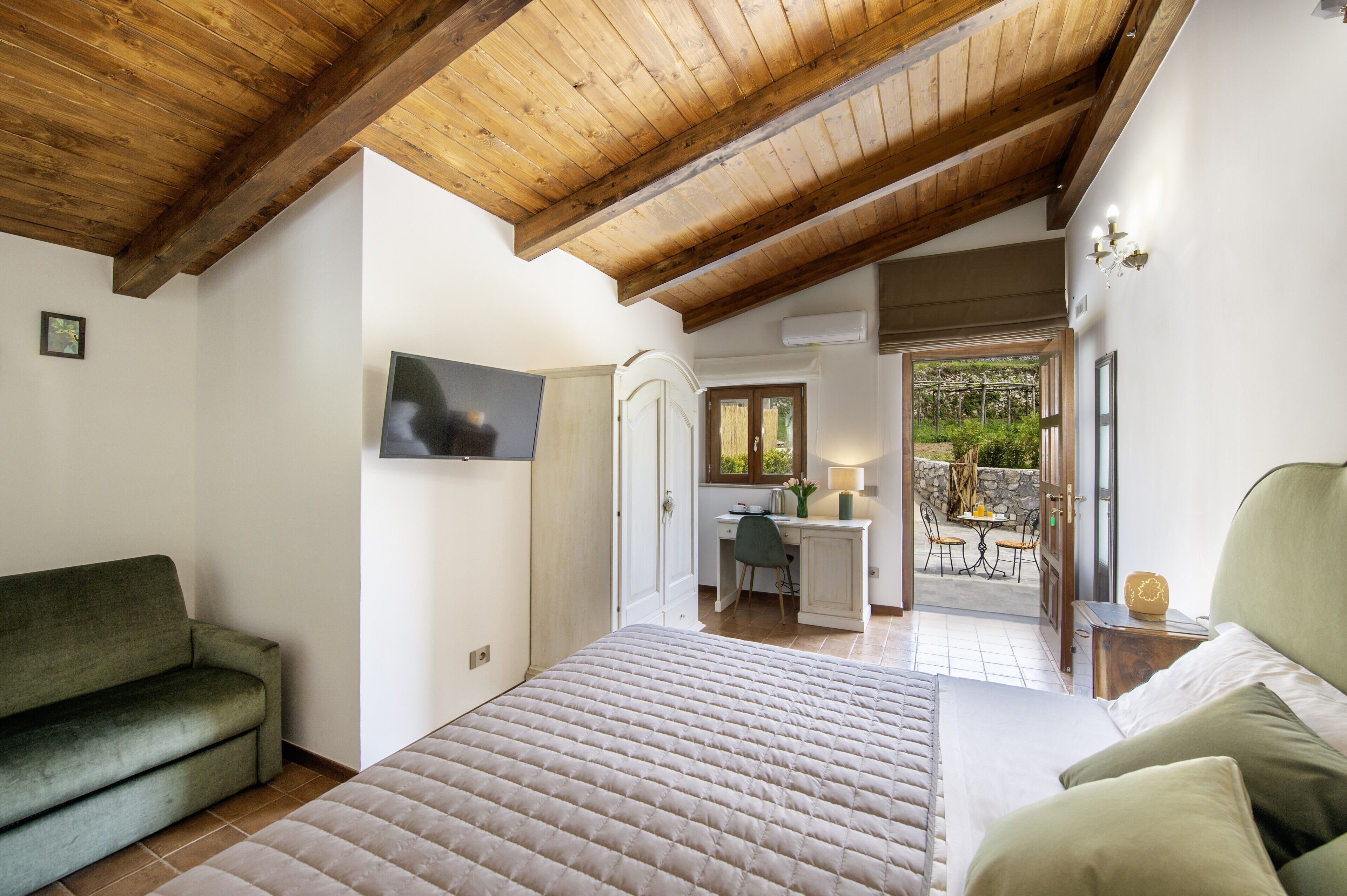 A bedroom with a bed, a green sofa, a desk, and a window.