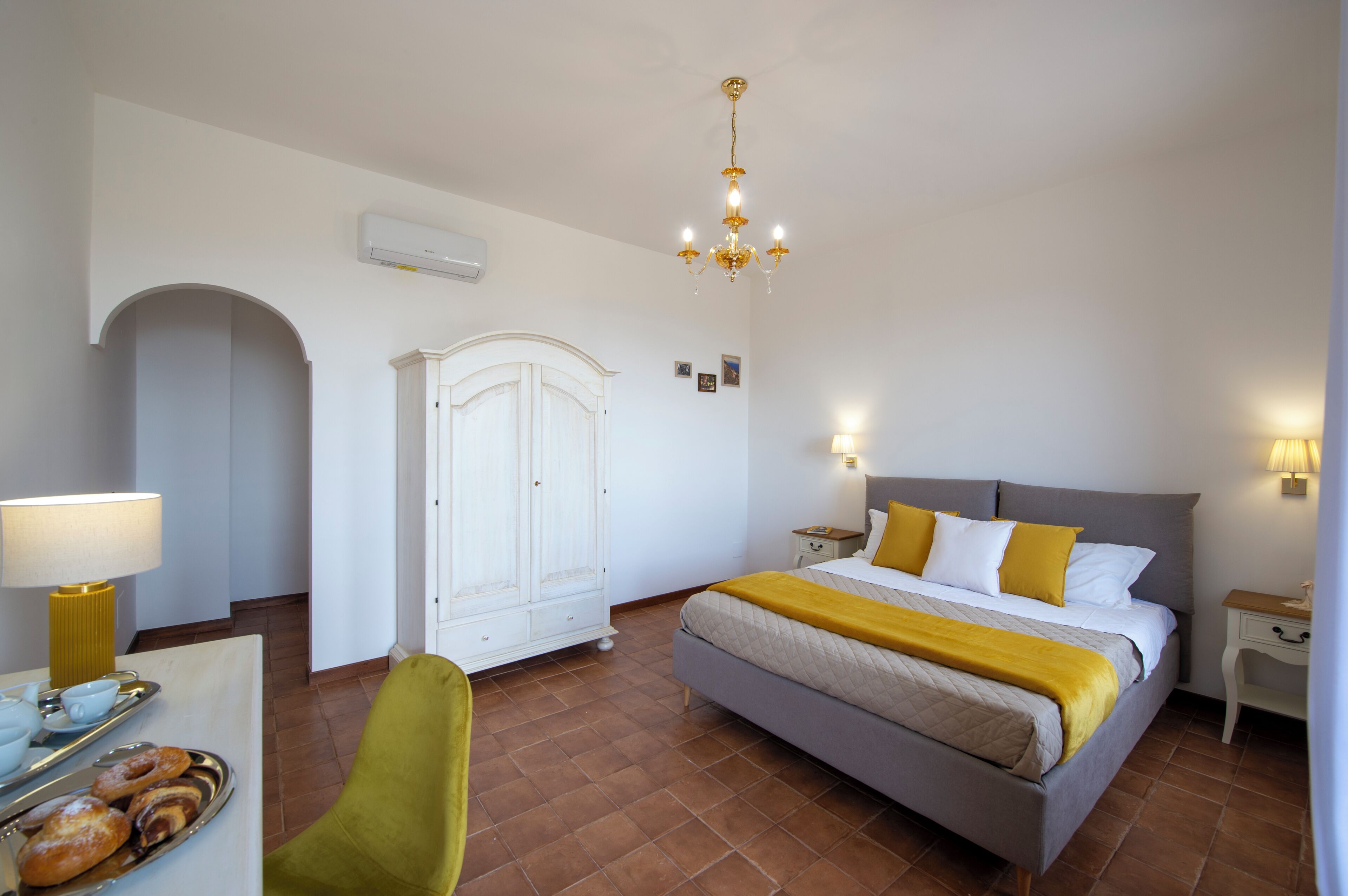 A hotel room with a bed, a desk with a lamp, a chair, a wardrobe, and a breakfast tray.