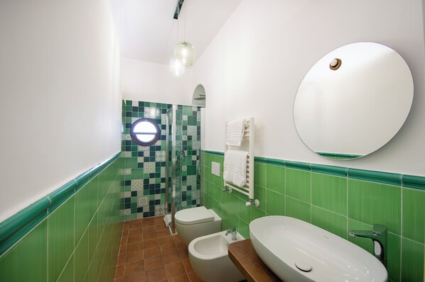 A bathroom with a green and white tiled wall, a round mirror, a white sink, and a toilet. - IL vigneto di nonno Pietro (Pianillo)