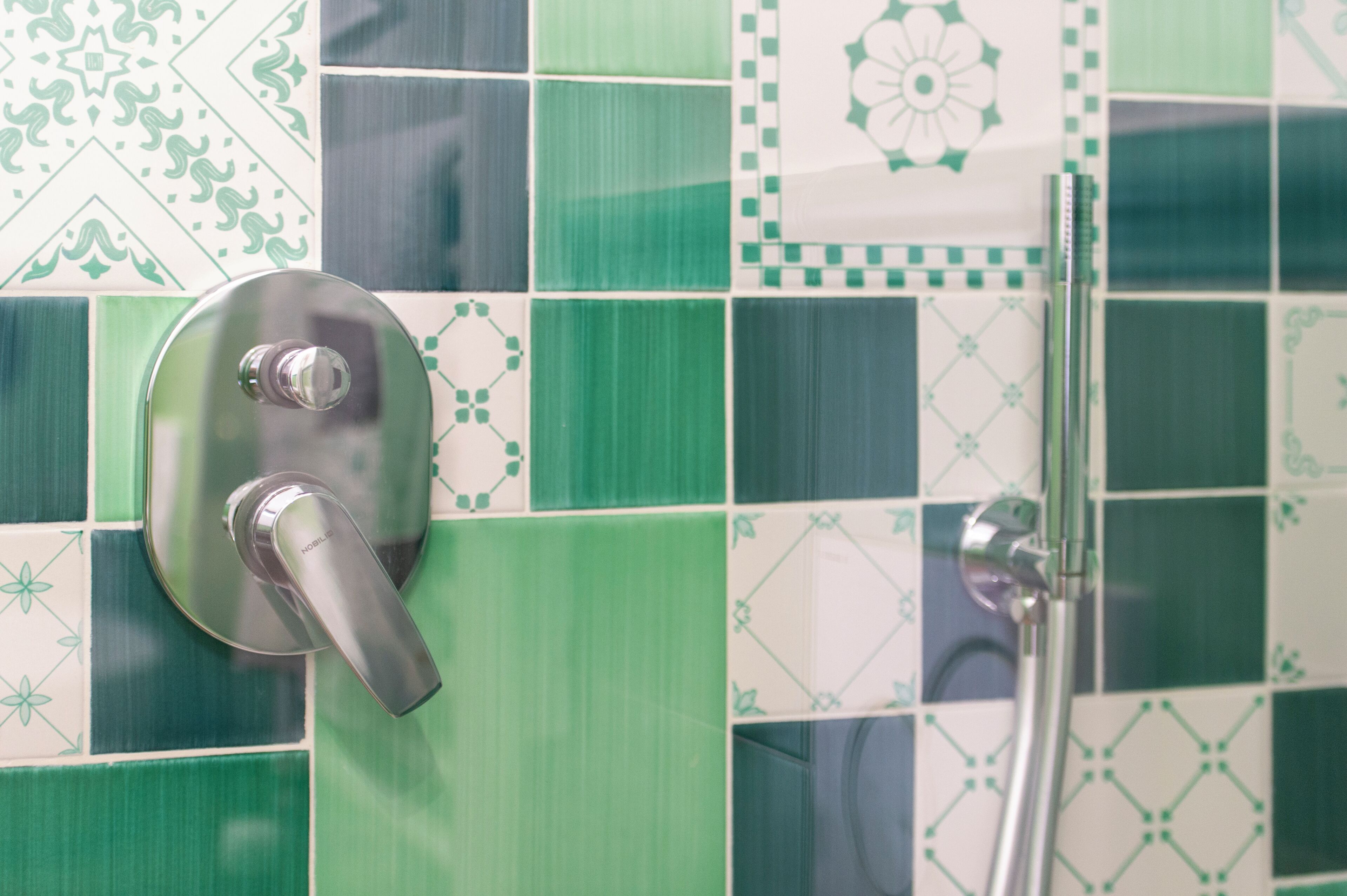 Ein Badezimmer mit modernem Wasserhahn und Duschkopf, gefliesst mit grün-weissen Mustern.
