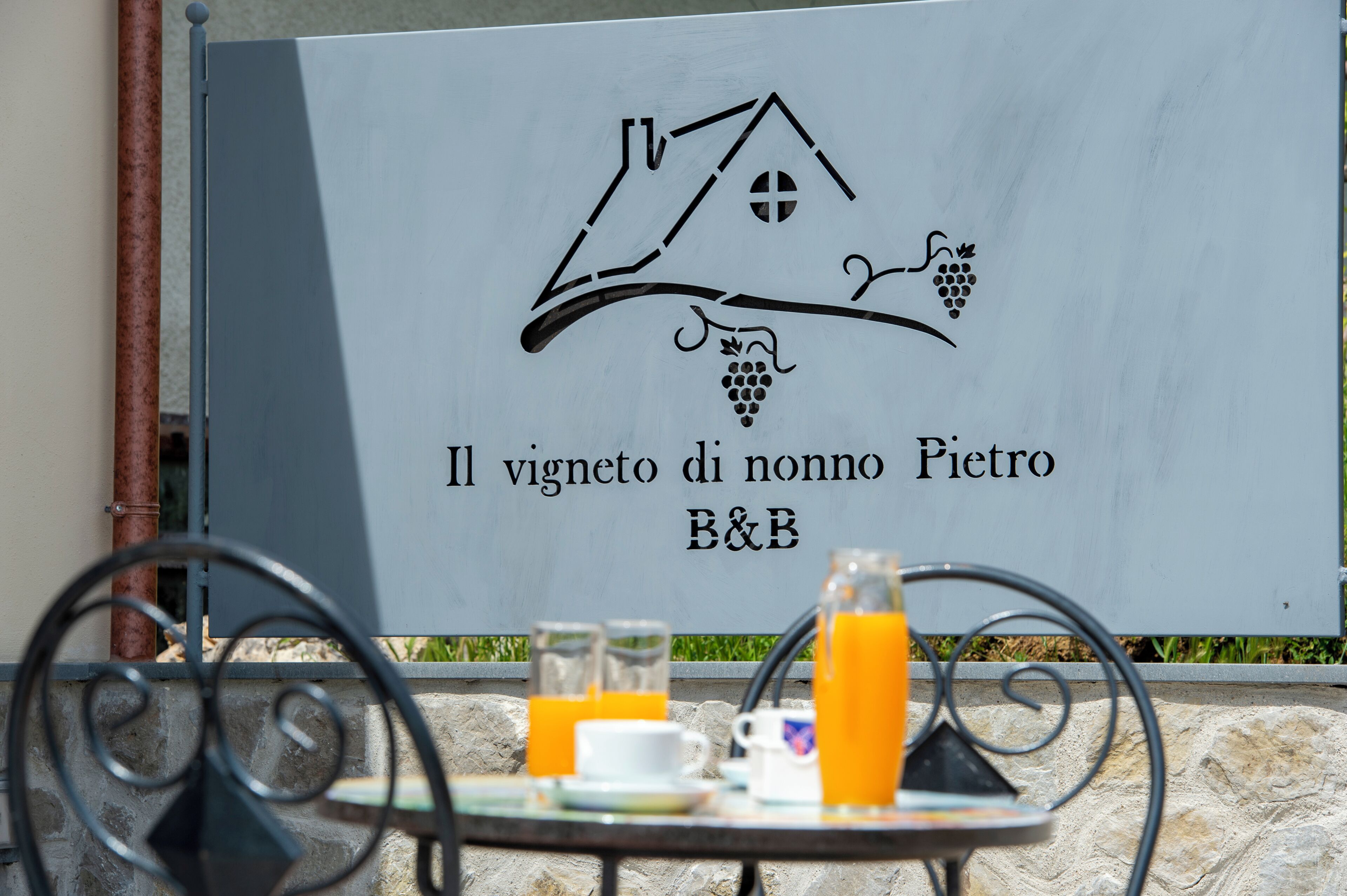 A sign with a house and grapes, indicating a vineyard hotel named Il vigneto di nonno Pietro B&B.