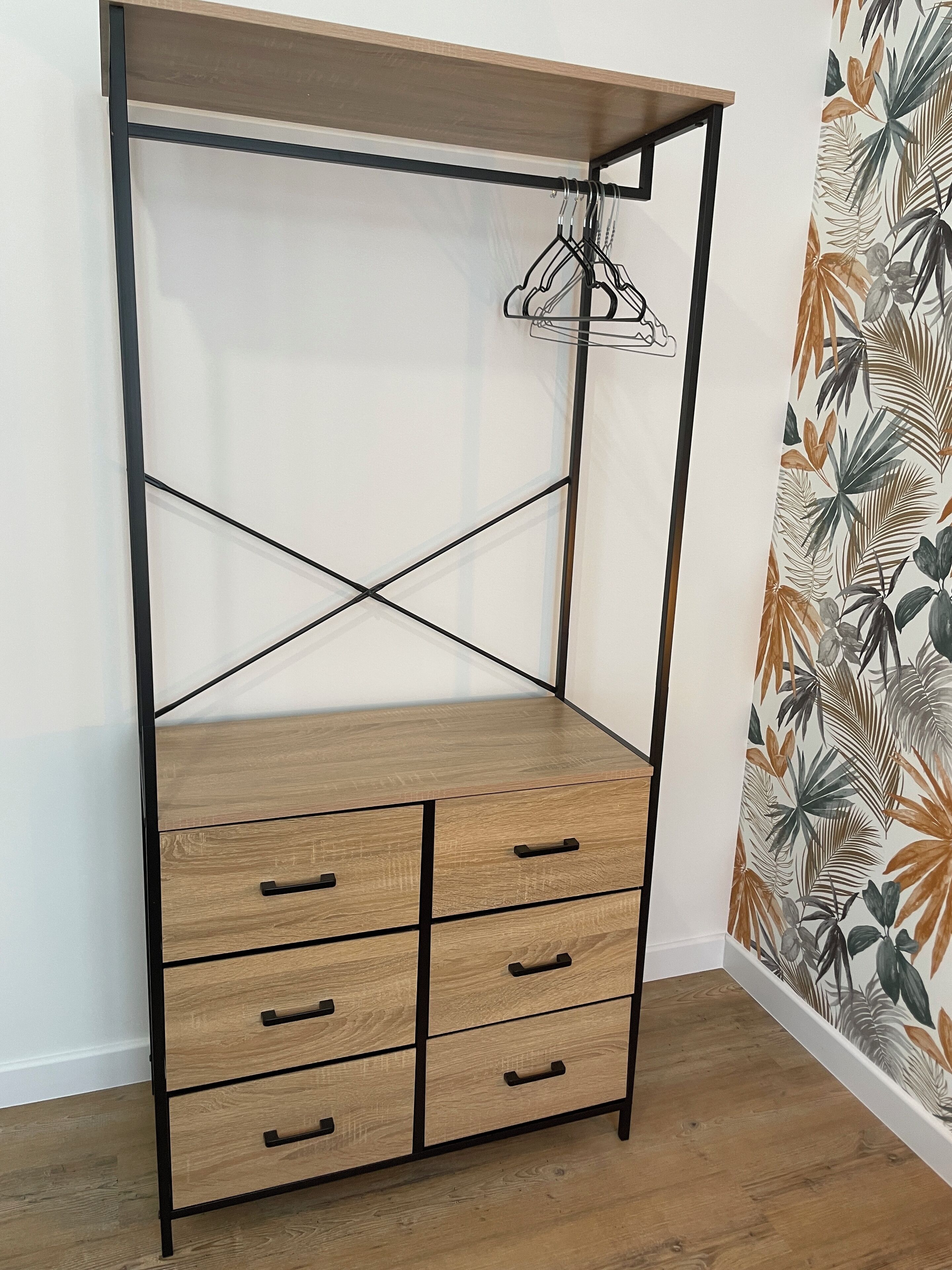 Une armoire en bois dotée d’une structure métallique, de nombreux tiroirs et d’un espace pour suspendre les vêtements.
