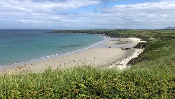 Eine Küstenlandschaft mit Sandstrand, grünen Hügeln und blauem Himmel.