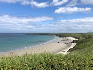 Eine Küstenlandschaft mit Sandstrand, grünen Hügeln und blauem Himmel.