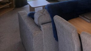 Ein Wohnzimmer mit grauem Sofa, einem kleinen Tisch und einem Balkon mit Vorhängen.