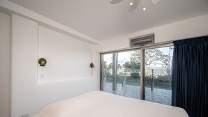 Une chambre moderne avec un grand lit, une porte-fenêtre coulissante donnant sur un patio et un ventilateur de plafond.