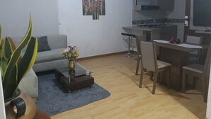 Un espace de vie compact comprenant un canapé, une table à manger avec des chaises, un petit coin cuisine et un vase décoratif avec des fleurs.