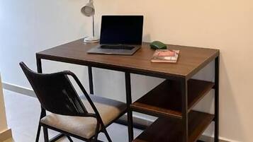 A small workspace with a laptop, a chair, and a framed picture on the wall.