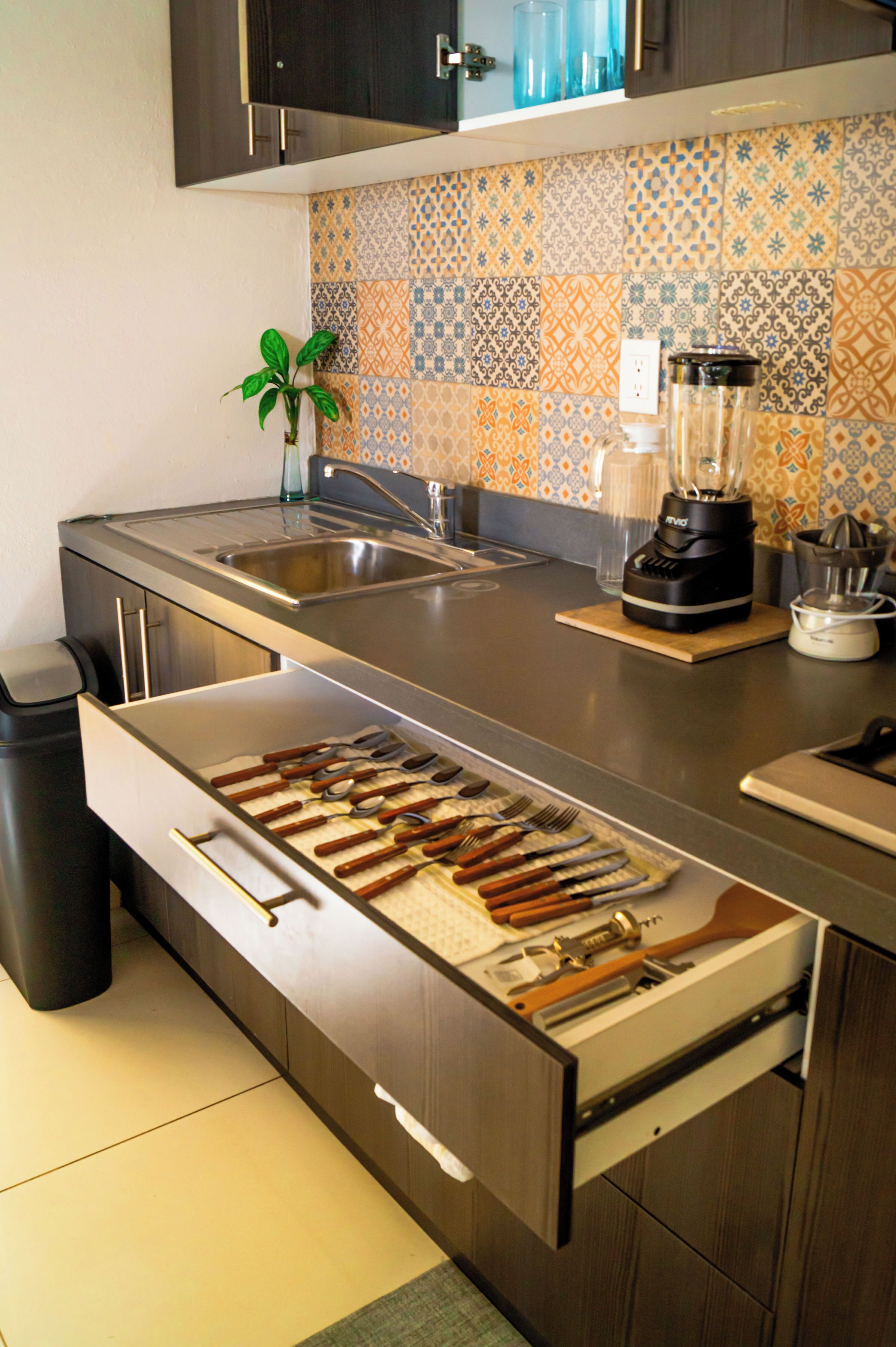 A kitchen with a built-in utensil drawer, a blender, and a tiled backsplash.