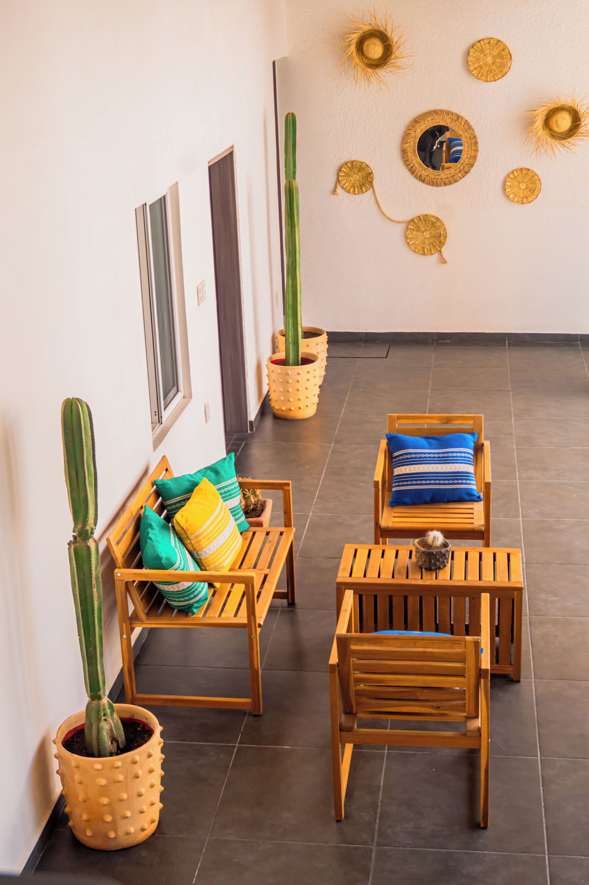 A sunlit patio with wooden furniture, potted cacti, and decorative wall art.