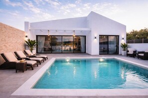 Ein moderner Poolbereich mit rechteckigem Pool, Liegestühlen und einer patioartigen Glasveranda.