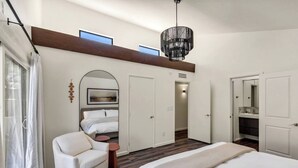 A modern bedroom with a large bed, a white armchair, a small table, and a walk-in closet. - Desert Luxe: 3BR W/Pools, Tennis (Tucson)