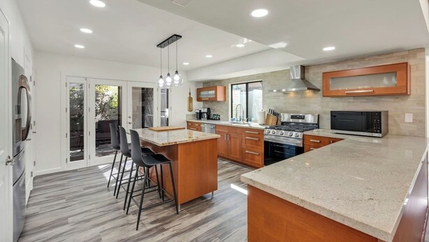 A modern kitchen with a large island, stainless steel appliances, and a sliding glass door leading to a patio. - Desert Luxe: 3BR W/Pools, Tennis (Tucson)