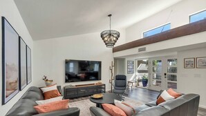 A modern living room with a large flat-screen TV, leather sofas, and a dining area with a table and chairs. - Desert Luxe: 3BR W/Pools, Tennis (Tucson)