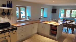 A kitchen with white cabinets, a wooden countertop, and a built-in island with a sink. There are windows providing natural light and a view of the outside. - Canal-side 5-bed Cottage - Sleeps 10, Pet Friendly (Stoke-on-Trent)