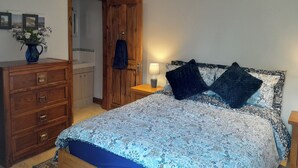 A bedroom with a bed, a dresser, a nightstand, a lamp, and a wooden door. - Canal-side 5-bed Cottage - Sleeps 10, Pet Friendly (Stoke-on-Trent)