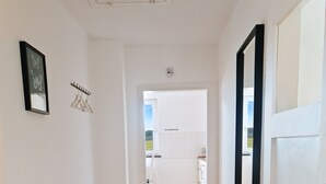 Un pasillo con piso de madera tipo espiga que conduce a una habitación con un espejo grande y una puerta.