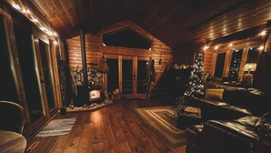 Interior acogedor de una cabaña de troncos con chimenea de piedra, un árbol de Navidad, muebles de cuero y techo de madera.