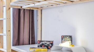 Un lit superposé avec un bureau en dessous, un petit tabouret et une boîte à jouets sur le bureau.