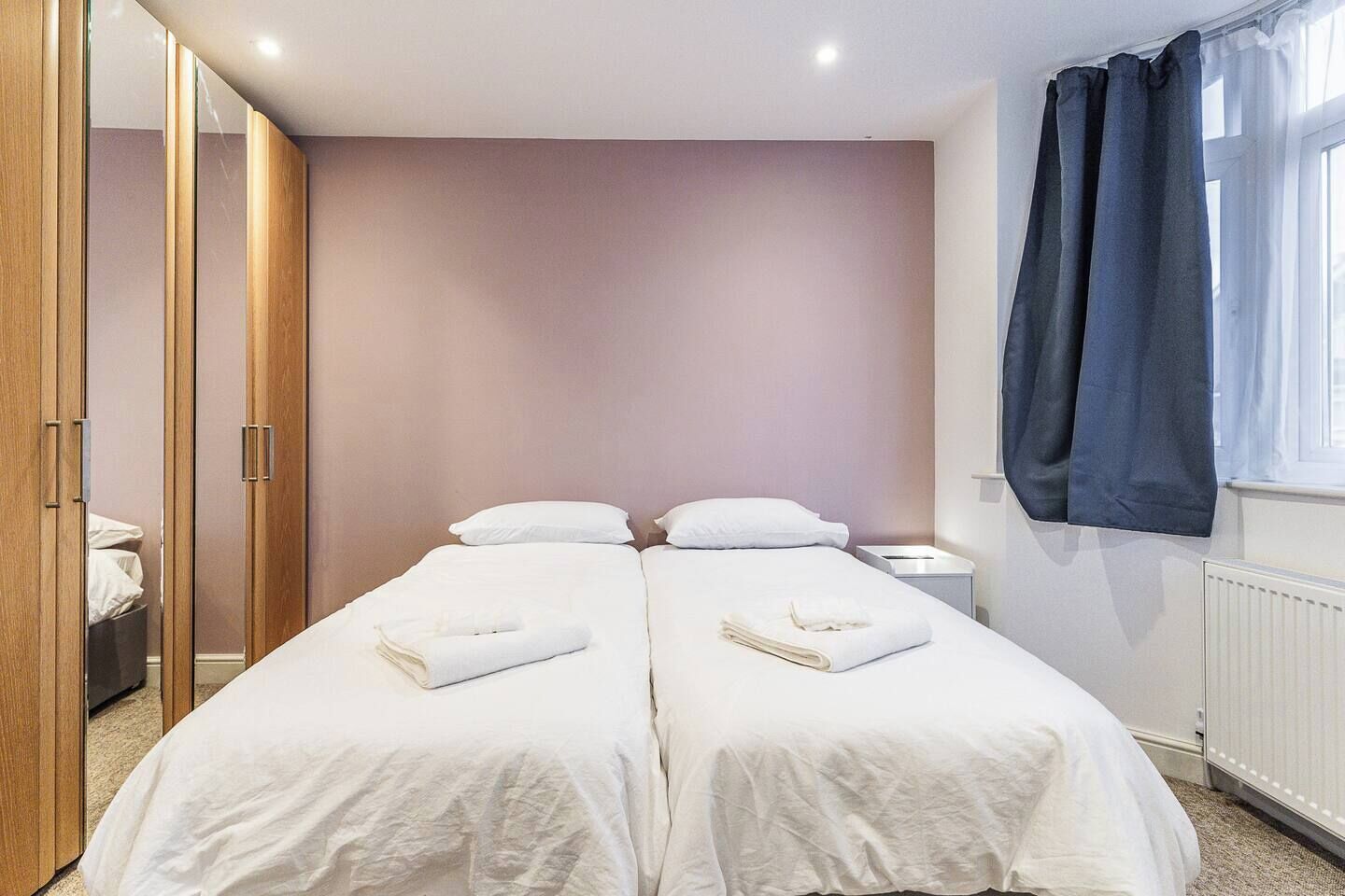 Ein Doppelbett mit weißer Bettwäsche, ein Nachttisch, ein Spiegel und ein Kleiderschrank mit Schiebetüren.