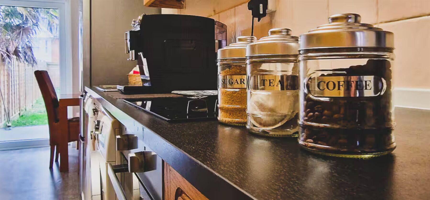 Uma bancada de cozinha com cafeteira, açúcar, chá e recipientes para café.