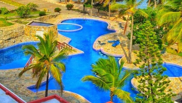 A resort with a large pool, palm trees, and a view of the ocean. - Shanzu Oceanfront Apartments (Mombasa)