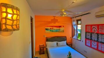 A bedroom with a bed, a ceiling fan, a wall-mounted light fixture, a painting, and a window with curtains.